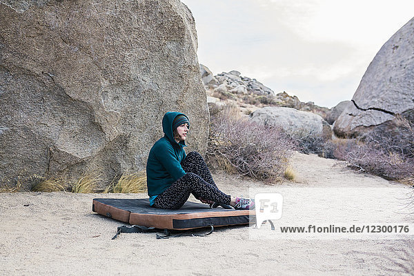 Woman putting on rock climbing shoes while getting ready to warm up on Iron Man Traverse v4  Bishop  California  USA
