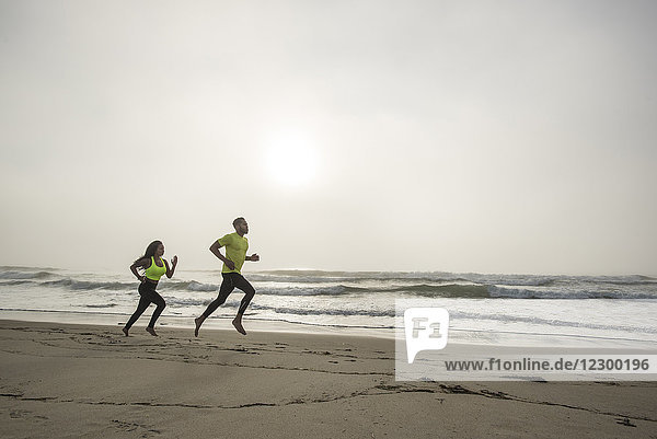 Side view of man and woman jogging on beach
