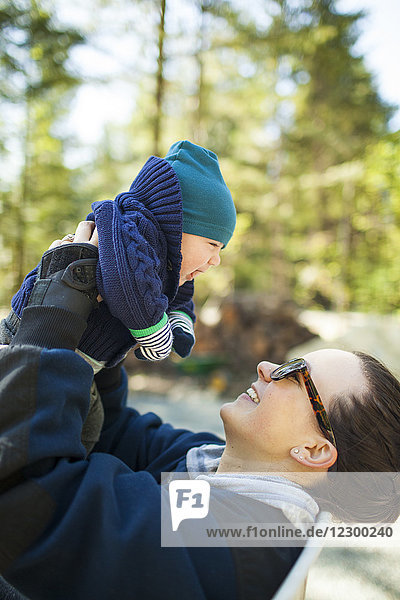 Seitenansicht einer Mutter  die ein Baby mit Strickmütze und Pullover in die Höhe hält
