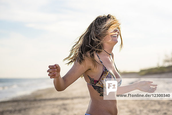 Taillenaufnahme einer jungen lächelnden Frau im Bikini am Strand