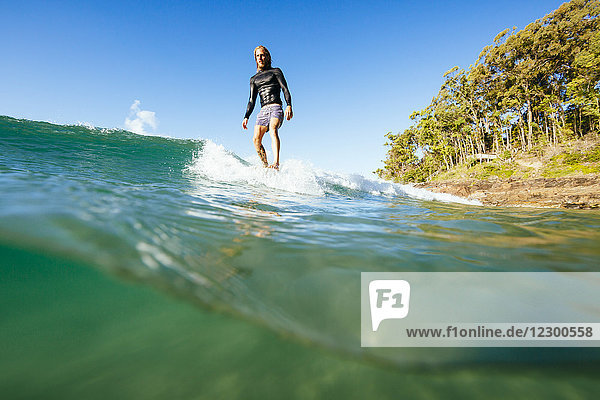 A man surfing with his toes on the nose of a longboard on a wave on a sunny day at Noosa National Park.