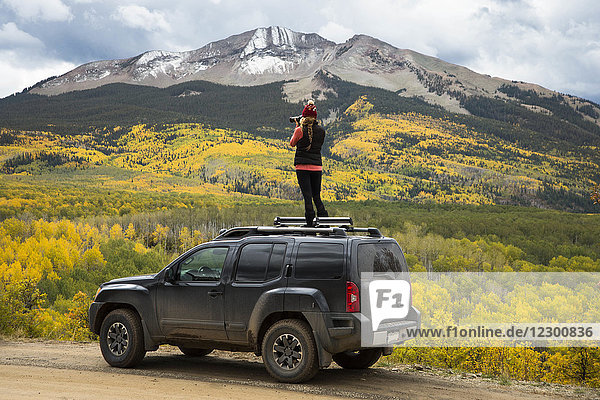 Woman photographing autumn scenery with mountain from top of 4x4 car  Crested Butte  Colorado  USA