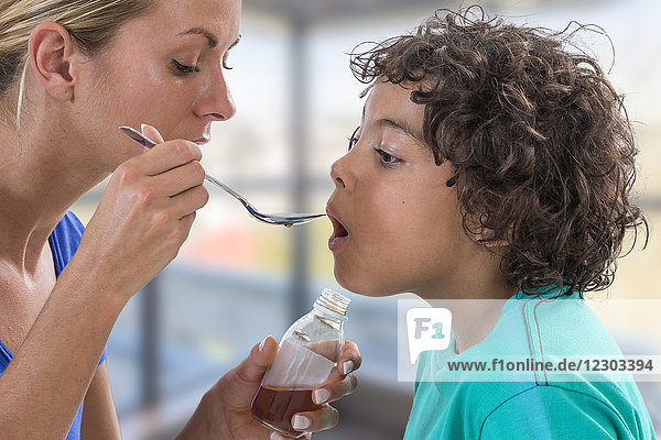 Mother giving her son a spoon of medicine.