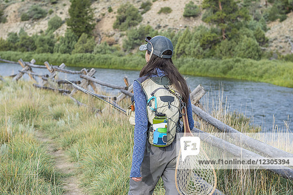 Female angler walking along fence beside Colorado River with backpack and fishing net Colorado USA