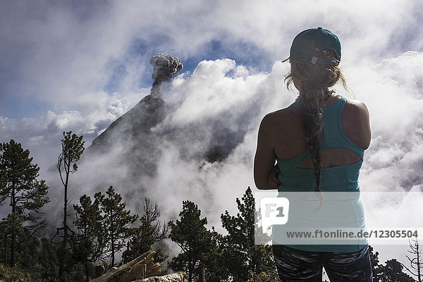 Rear view shot of young female hiker looking at view of Fuego Volcano  Guatemala