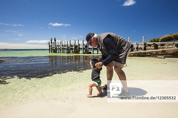 Seitenansicht des Großvaters  der mit einem kleinen Jungen am Strand spielt