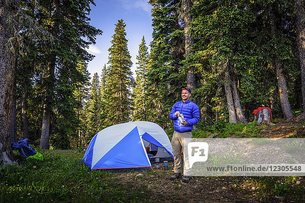 Vorderansicht  Ganzaufnahme eines einzelnen männlichen Rucksacktouristen  der beim Zelten im Wald isst  Colorado Trail  Colorado  USA