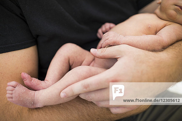 Nahaufnahme der Hände des Vaters  der ein nacktes Neugeborenes hält