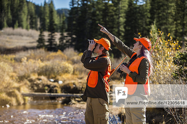 Male hunter looking through binoculars at target pointed by female partner  Colorado  USA