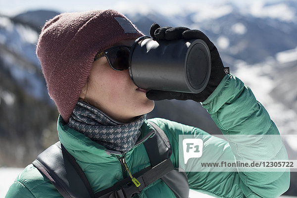 Kopf- und Schulteraufnahme einer Frau  die beim Schneeschuhwandern im Winter in der Nähe von Aspen  Colorado  USA  Kaffee aus einem Becher trinkt