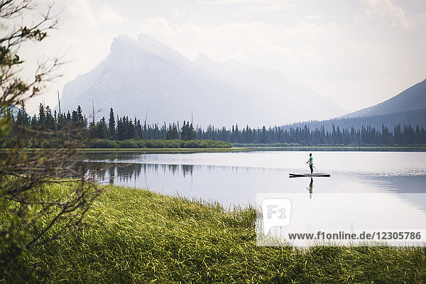 Woman paddleboarding across one of Vermillion Lakes with Mount Rundle in background  Alberta  Canada