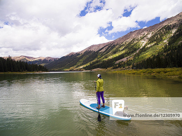 Woman paddling with her dog on paddle board at reservoir in mountains near Aspen  Colorado  USA