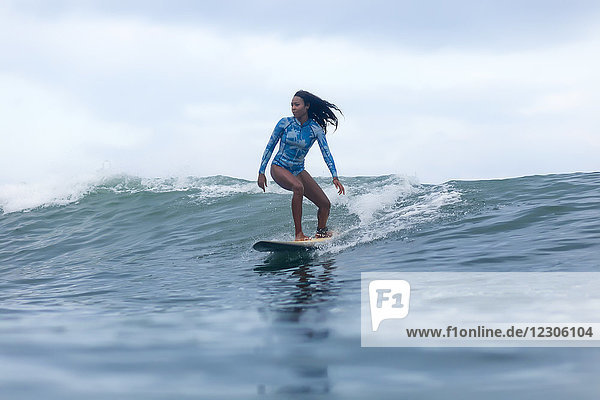 Totale Aufnahme einer einzelnen Frau  die auf einem Surfbrett im Meer auf einer Welle reitet