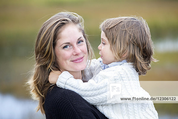 Kopf-Schulter-Porträt einer lächelnden Mutter  die ihren Sohn in einer natürlichen Umgebung hält