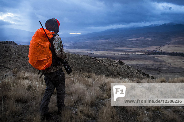 Hirschjäger geht mit Gewehr durch das Hinterland von Colorado bei Sonnenaufgang  während sich ein Gewitter nähert  Colorado  Colorado  USA