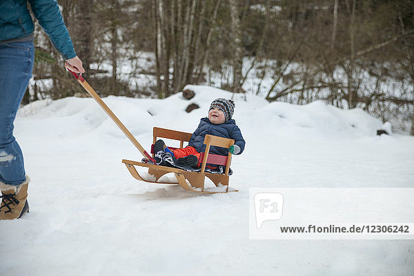 Mutter spielt im Winter mit ihrem Sohn im Freien  indem sie ihn auf einem Schlitten zieht
