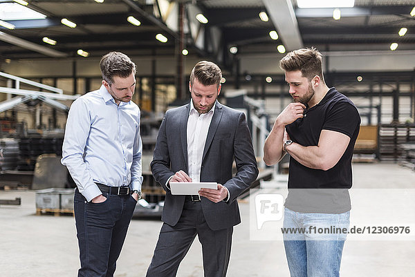 Three men sharing tablet on factory shop floor