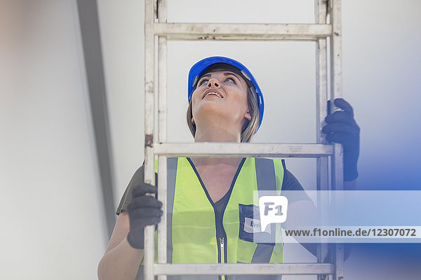 Young woman on construction site climbing ladder