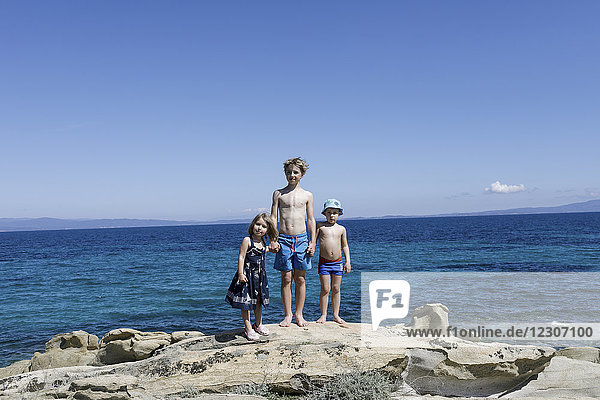 Griechenland,  Chalkidiki,  drei Kinder,  die Hand in Hand auf Felsen vor dem Meer stampfen