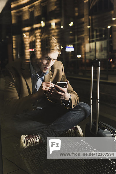 Businessman using cell phone at tram station at night