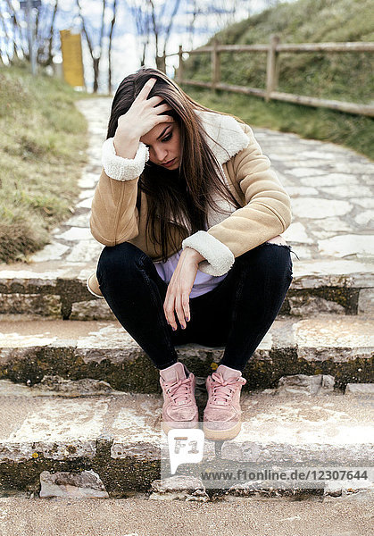 Traurige junge Frau im Freien auf einer Treppe sitzend