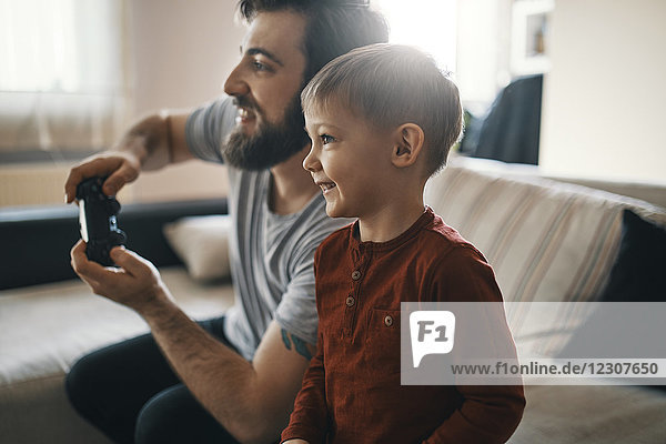 Happy little boy playing computer game with his father at home