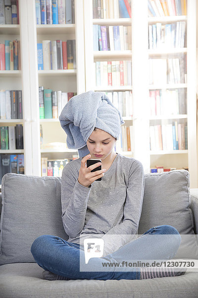 Mädchen mit Handtuch Turban sitzend auf der Couch zu Hause beim Blick auf das Handy