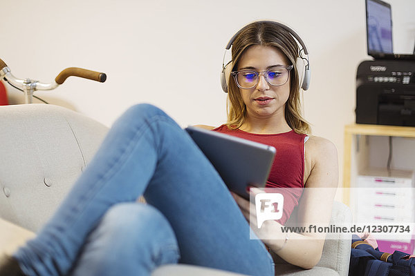 Lässige junge Frau mit Kopfhörer mit Tablett im Coworking Space
