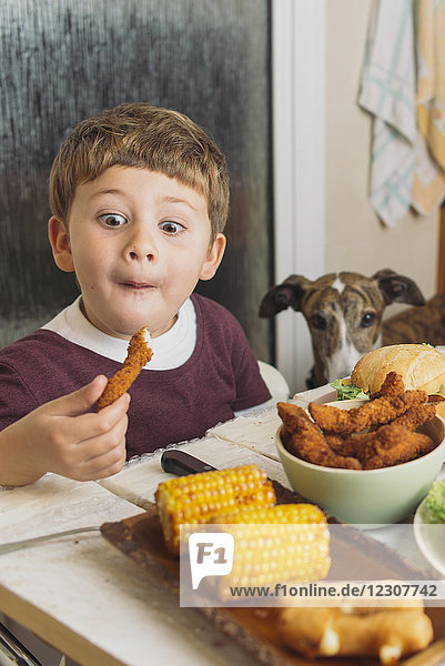 Boy with dog enjoying american food at dining table at home