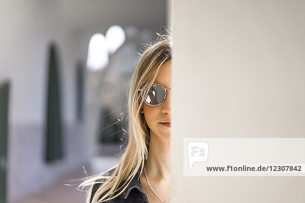 Portrait of young woman wearing mirrored sunglasses hiding behind column
