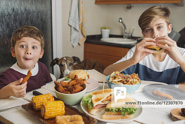 Zwei Jungen mit Hund genießen amerikanisches Essen am Esstisch zu Hause