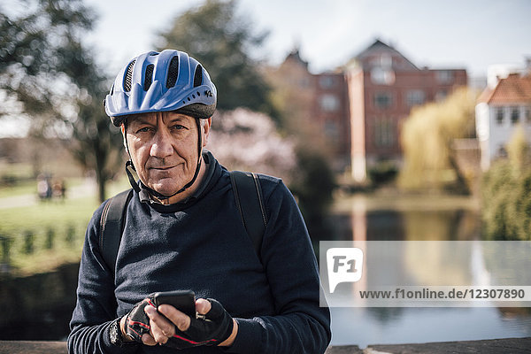 Portrait eines älteren Mannes mit Fahrradhelm mit Smartphone