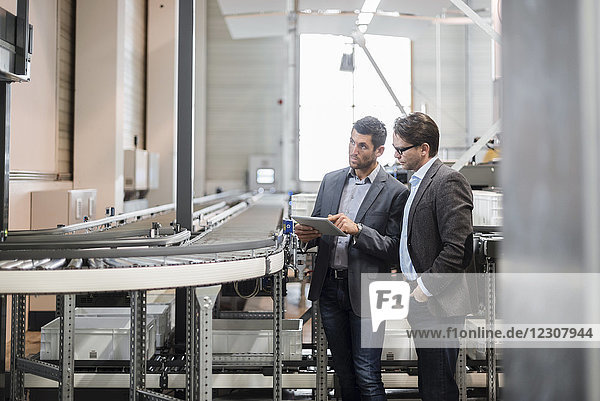 Two businessmen with tablet talking at conveyor belt in factory