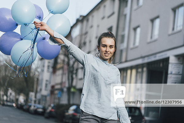 Porträt einer lächelnden Frau mit blauen Luftballons auf der Straße