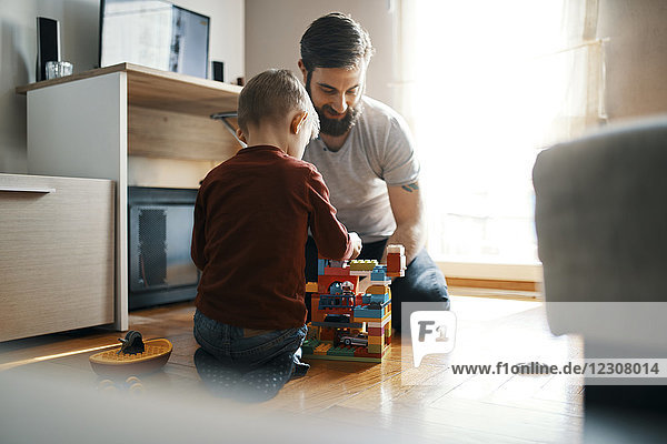 Father and son sitting on the floor at home playing together with building bricks