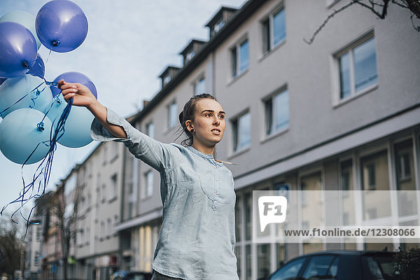 Porträt einer jungen Frau mit blauen Luftballons im Freien