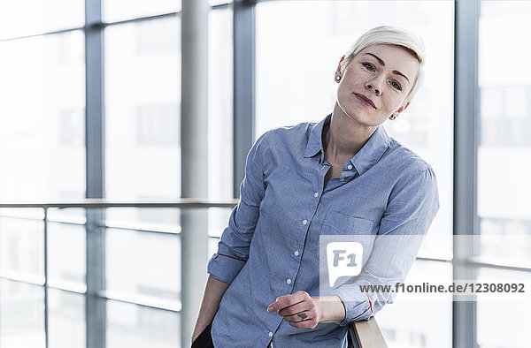 Porträt einer Frau im Bürogebäude  die sich am Geländer lehnt