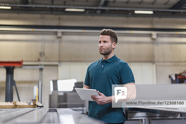 Man with tablet on factory shop floor looking around