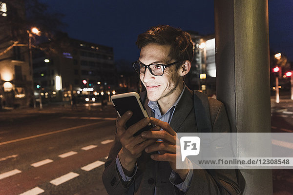 Lächelnder Geschäftsmann mit Handy in der Stadt bei Nacht