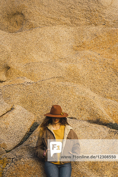 Frau mit Hut an der Felswand lehnend