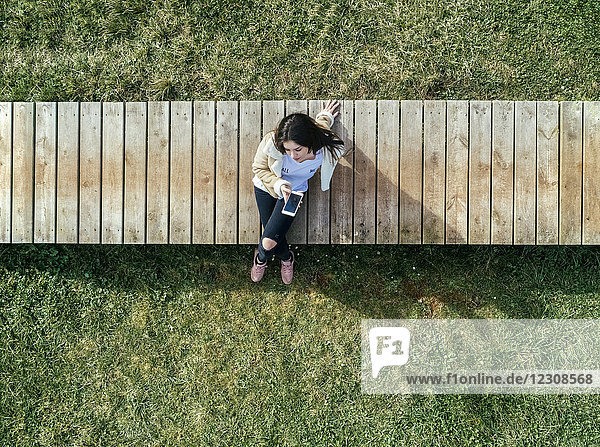 Young woman sitting on boardwalk checking her smartphone