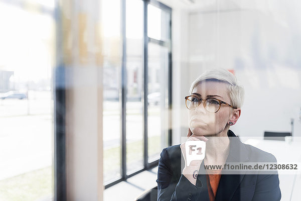 Fokussierte Geschäftsfrau beim Blick auf die Glasscheibe im Büro
