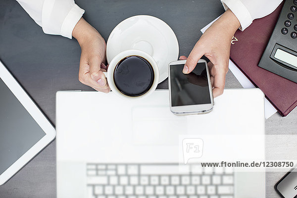 Woman with cup of coffee using smartphone laptop