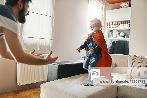 Vater spielt mit seinem kleinen Sohn  verkleidet als Superheld zu Hause.