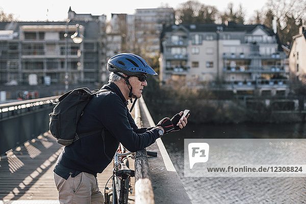 Senior Mann mit Fahrradhelm mit Smartphone auf der Brücke