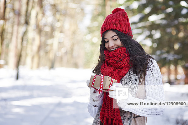 Portrait of happy young woman with Christmas gift in winter forest