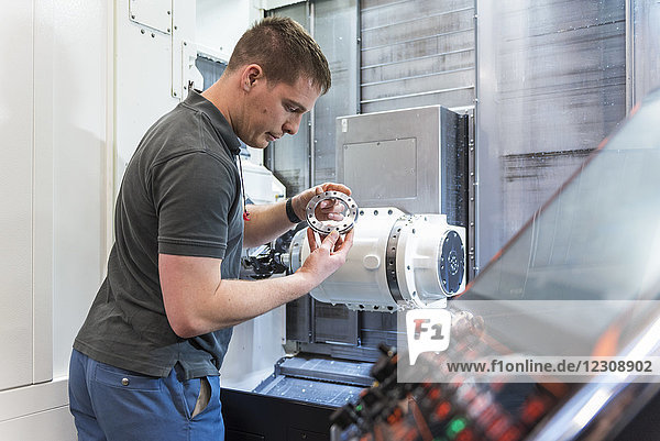 Man examining workpiece at machine in factory