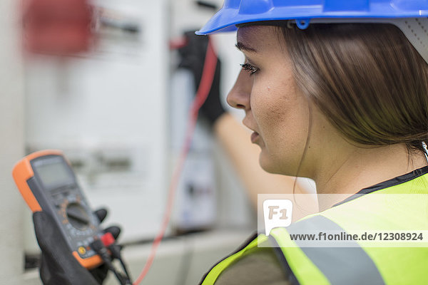 Young female electrician working with voltmeter at fusebox