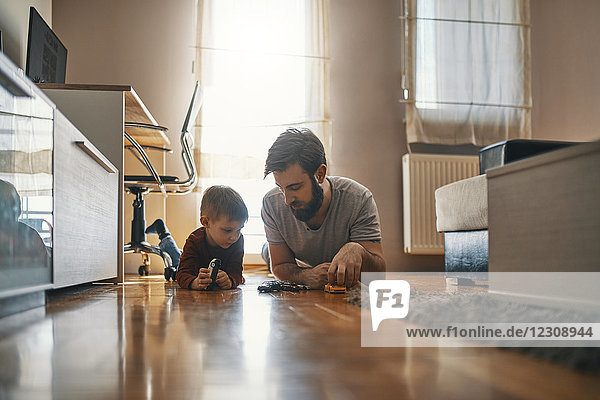 Vater und Sohn liegen zusammen auf dem Boden und spielen mit Spielzeugautos.