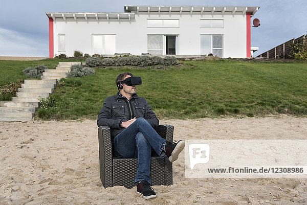 Mann im Sessel am Strand sitzend mit VR-Brille